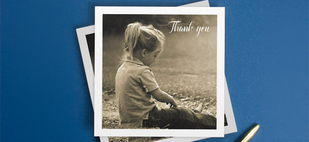 A personalised communion photo thank you card. The card is square and printed with a photo of a young girl. The white card sits on a blue background.