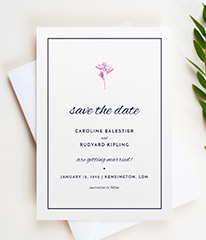 A classic wedding save the date design. The save the date card has a traditional blue border, surrounding a simple flower motif and elegant text.