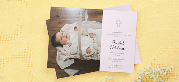 A religious christening invitation card with a photo of a baby girl. The invite is printed with a purple crucifix.