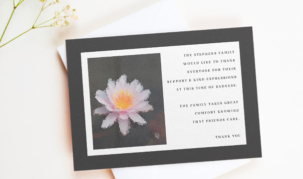 A thank you card for after a funeral. It has a painted white lily and a black border. There is a personalised message from the family on the right.