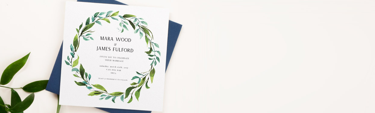 A customised wedding invitation design. This wedding invitation is printed with a green watercolour wreath design. The card sits on a blue envelope.