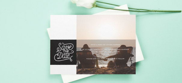 A wedding save the date design, printed with a photo of the engaged couple. “Save the Date” is stylistically written in white on a black background.