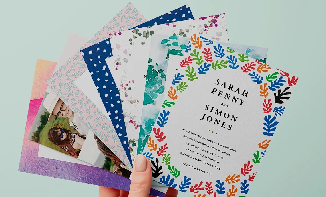 Lady's hand holding seven colorful and premium printed wedding invitations, showcasing diverse designs.
