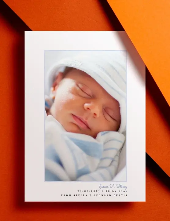A baby birth announcement card with printed toy animals sat on a brown envelope. The card shows a photo  and birth details of a new-born baby girl.