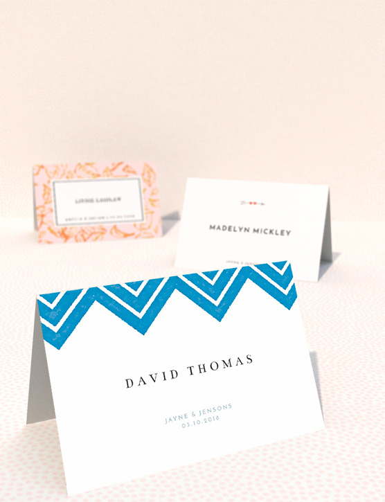 A table place card for weddings, personalised with a wedding guest’s name. It is a floral place card design, sat on a navy-blue background