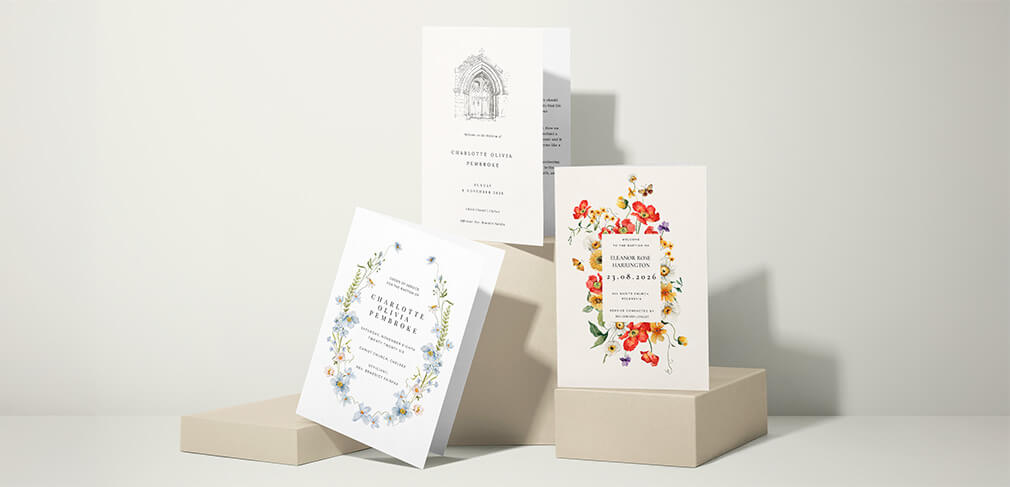 Three floral christening order of service booklets displayed on beige plinths