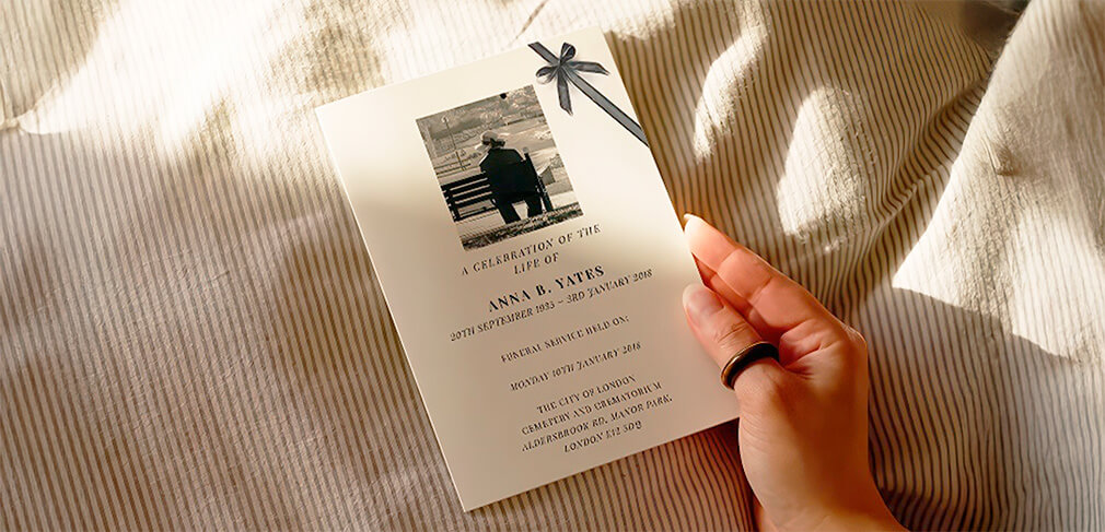 Hand holding funeral order of service booklet with photo and bow on striped fabric