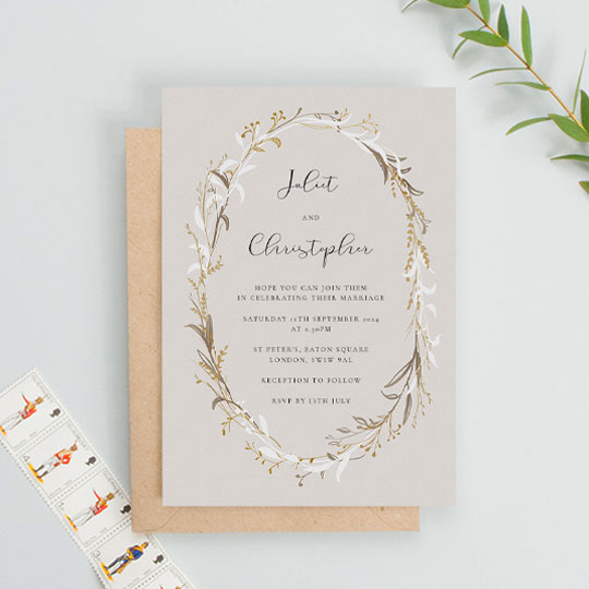 A rustic floral wedding invitation made of an unusual gold, white and brown wildflower wreath. This is a portrait wedding invitation with an earthy background and modern text.