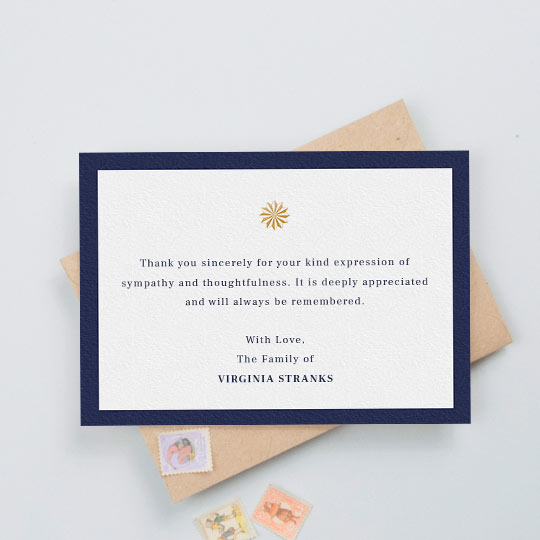 A funeral thank you card with a thick, navy blue border and an orange/gold sundial icon in the middle. The card has a personalised message of thanks in the middle