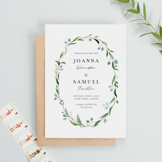 A floral, classic wedding save the date card. It is a white card with a green and blue watercolour floral wreath. In the middle of the floral wreath, the save the date has the details of a wedding printed.