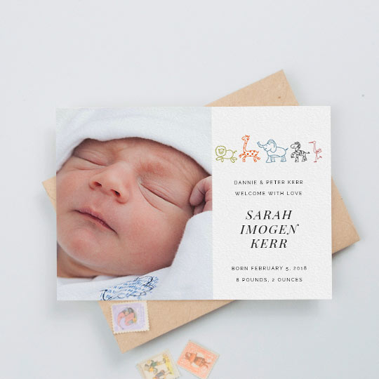 A cute baby birth announcement card with a large baby photo to the left, and cartoon safari animals drawn on the right. The baby’s birth details and a message from the parents are printed in black on the right-hand side.