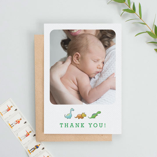 A portrait baby thank you card with dinosaurs underneath a baby photo. The photo on the thank you card takes up most of the design.