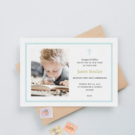 A first holy communion invitation for a young boy. It has a baby blue border and blue crucifix. The card has a photo of a boy on the left. His name is written in a gold font