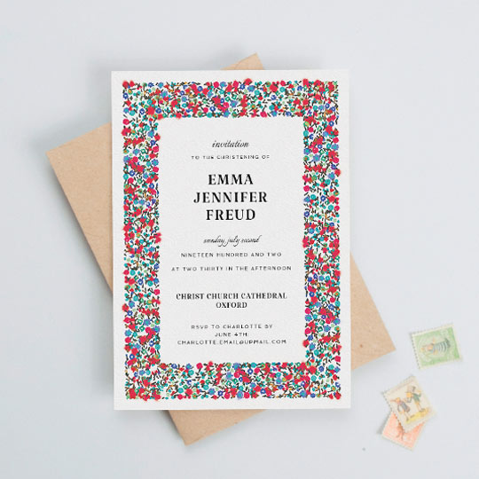 A white christening invitation card with a colourful red and blue floral border. There is black text in the middle with details of a baby girl and her christening.