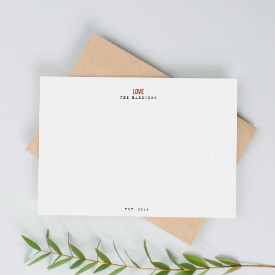 A white, personalised desk note card. It is personalised with the names of a couple and has the word “LOVE” printed in red at the top of the note card.