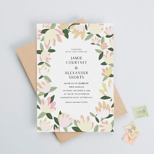 A modern floral wedding invitation design with dozens of pastel flowers and leaves forming a border around elegant wedding invitation text.