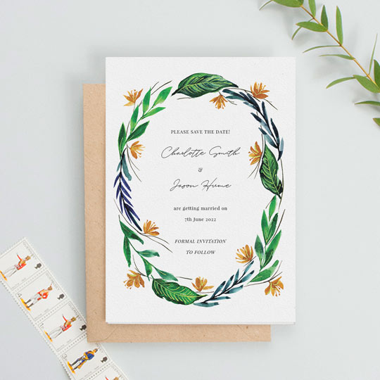 A modern, floral wedding save the date card with tropical leaved and flowers making up a painted wreath. The background of the save the date is white, and the information of an upcoming wedding is printed in the middle.