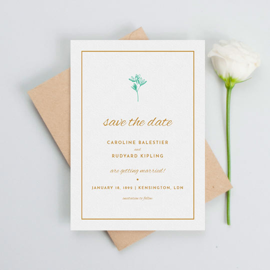 A simple wedding save the date design with a thin orange border and understated blue flower printed at the top of the card. The details of an upcoming wedding are printed in orange in a range of fonts.