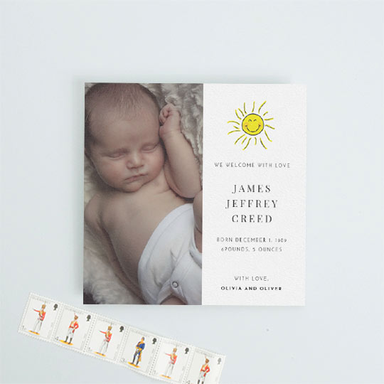 A square baby birth announcement card with a baby photo on the left-hand side. It has a hand drawn picture of the sun smiling on the right-hand side. The baby’s birth details are printed underneath the sun.