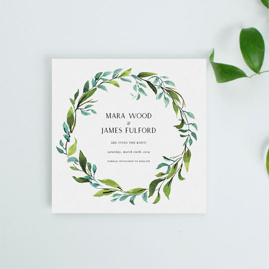 A classic, floral wedding save the date card. It is a square wedding save the date with a green and blue wreath around the outside. The floral wreath on the save the date card is hand painted in watercolour.