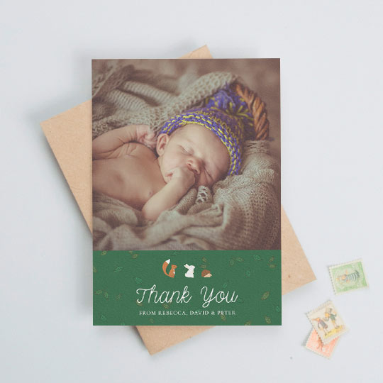 A baby thank you card with a baby photo at the top with a green, leaf-patterned section below. There are woodland animals above the words "thank you".