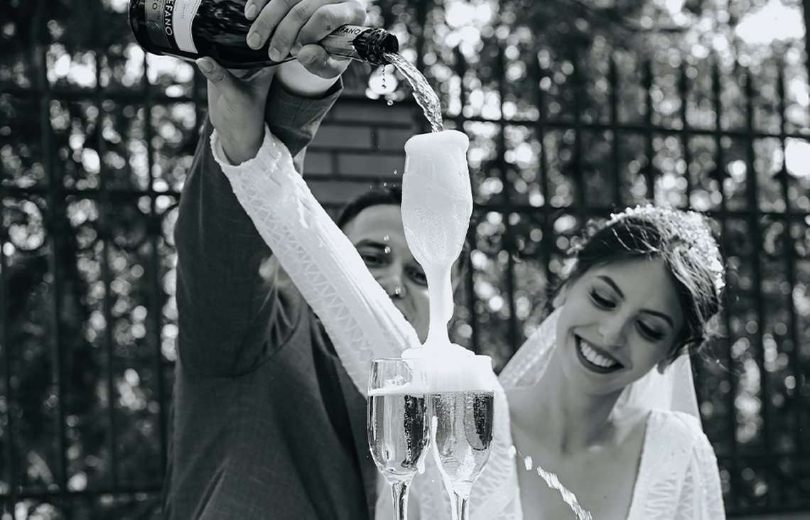 A black and white photo of a bride and groom with a champagne fountain in a garden.