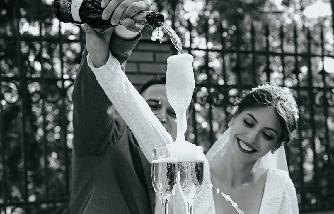 A black and white photo of a bride and groom with a champagne fountain in a garden. A black and white photo of a bride and groom with a champagne fountain in a garden.