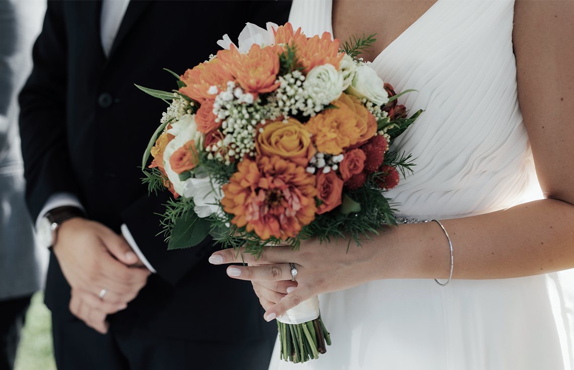 Photo of a couple in the process of getting married. Holding an orange bouquet at the ceremony.