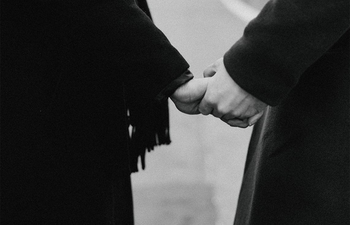 Friends holding hands at a funeral. Black and white photo.