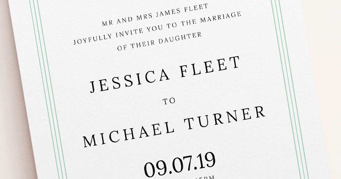 Close-up of a detailed green wedding invitation card with serif text and floral design.