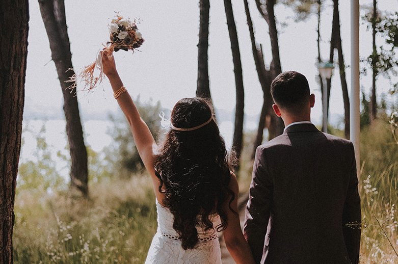 A view from behind a newly married couple. The bride is holding her bouquet aloft.