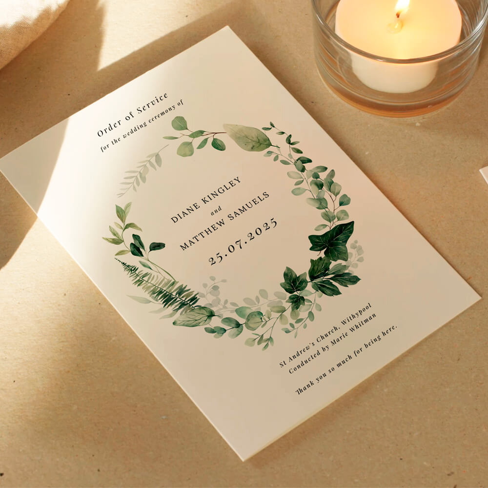 Wedding order of service booklet with a green wreath design, placed on a table beside a candle
